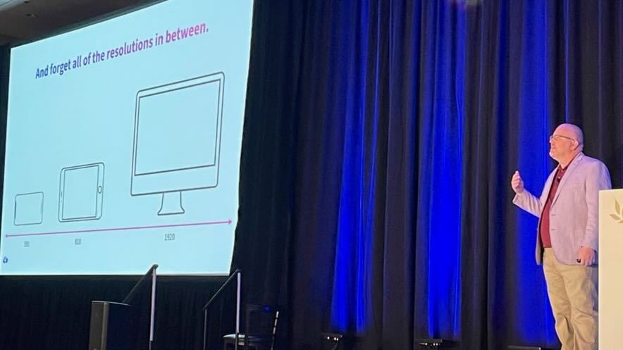 Jason Grigsby on stage at AEA Denver,
with a slide that shows outlines
of a phone, tablet, and desktop
with the headline
'And forget all of the resolutions in between'
